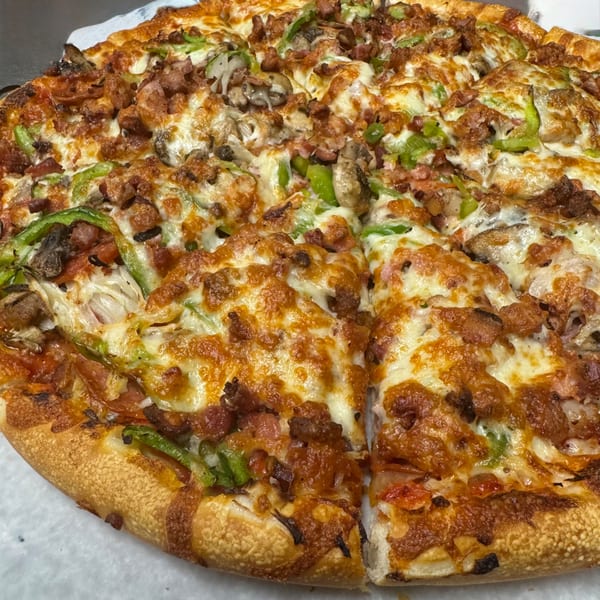 Milano's Pizza with melted cheese, green peppers, mushrooms, and meat toppings, with one slice removed.