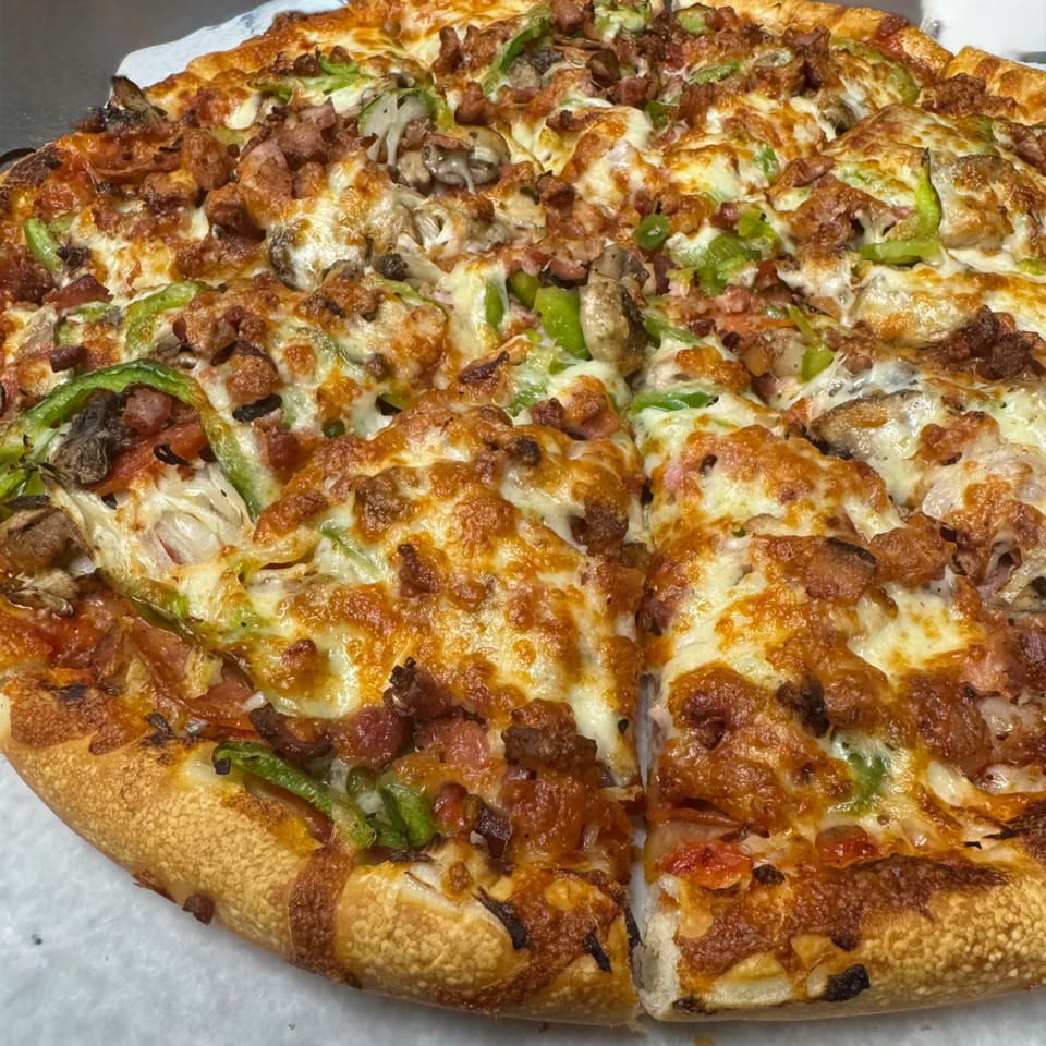 Milano's Pizza with melted cheese, green peppers, mushrooms, and meat toppings, with one slice removed.