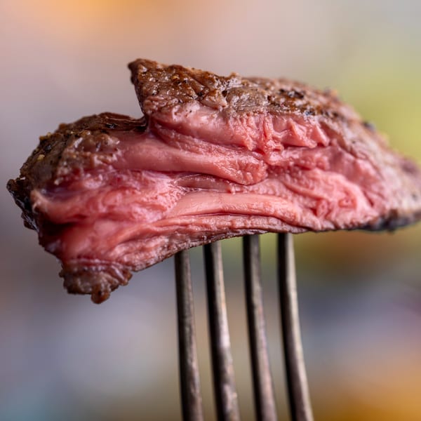 Close-up of a perfectly cooked, medium-rare steak slice on a fork, showing its juicy pink interior.